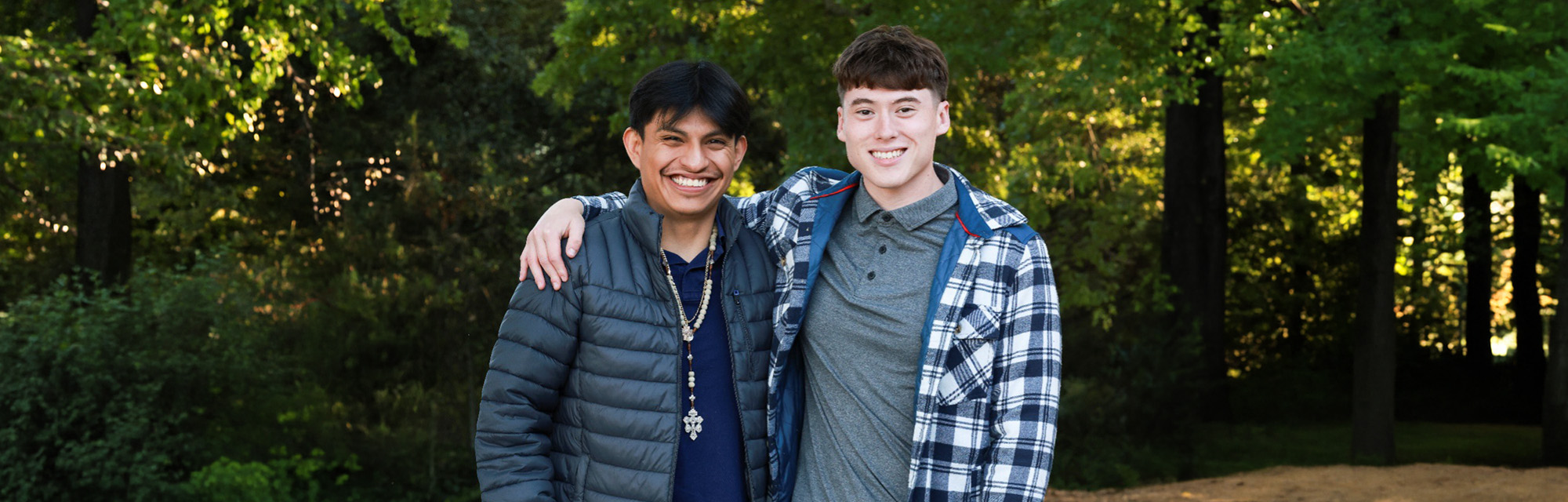Two people posing together outdoors with trees in the background.