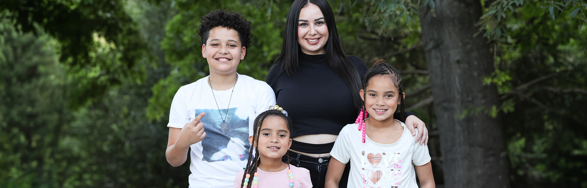 Adult and three children posing together outdoors in front of trees.
