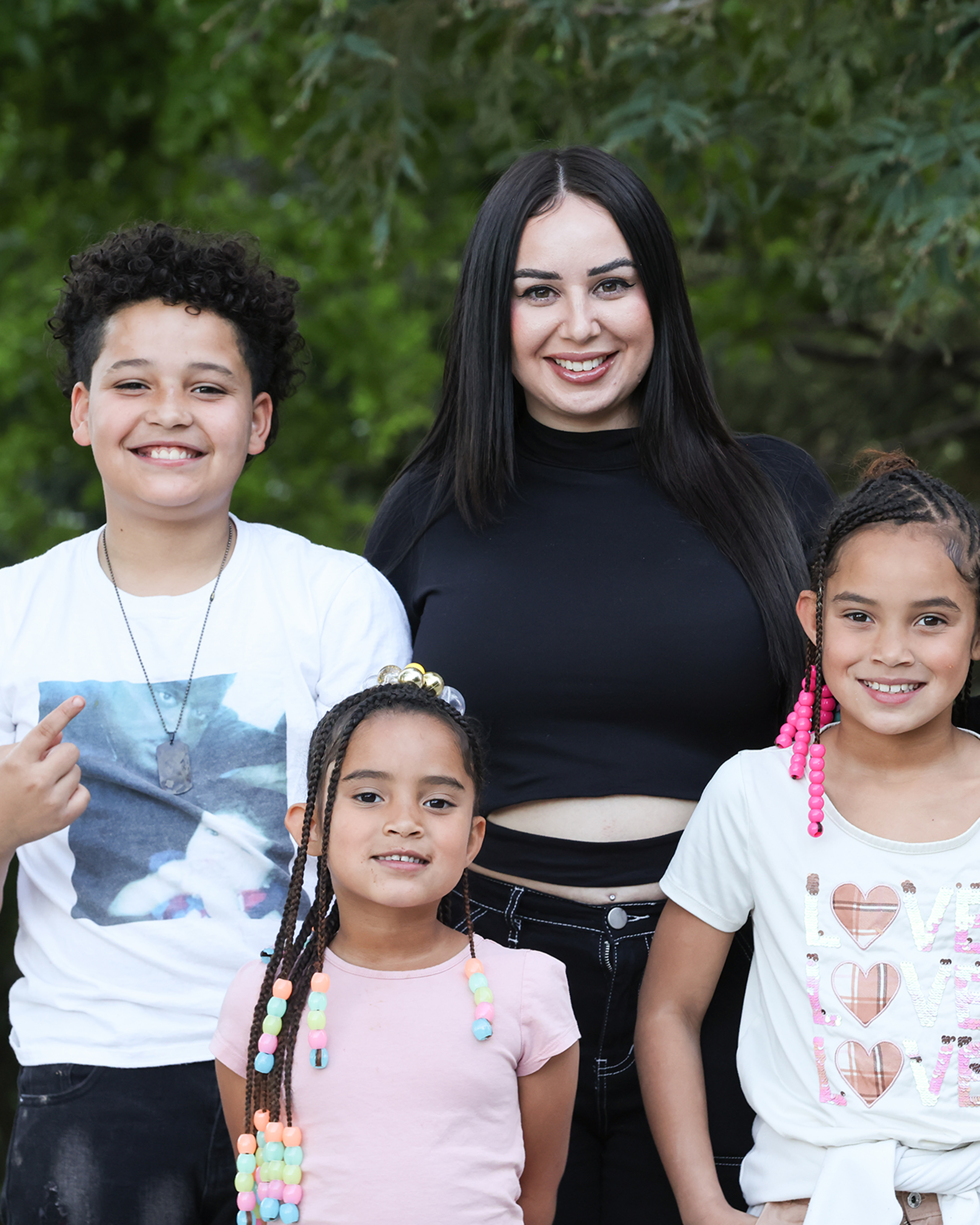 Adult and three children posing together outdoors in front of trees.