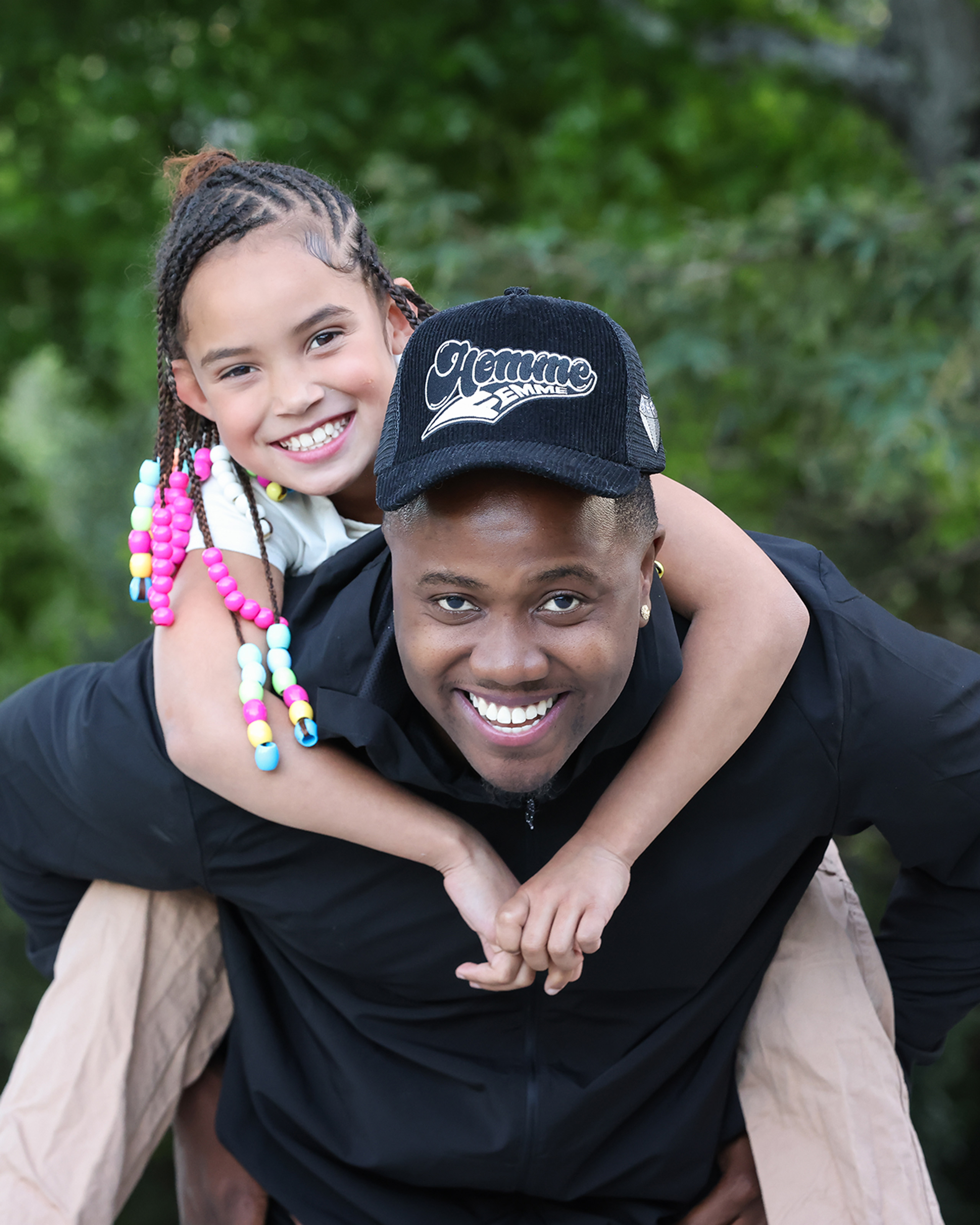 Person carrying a smiling child on their back outdoors in a wooded area.