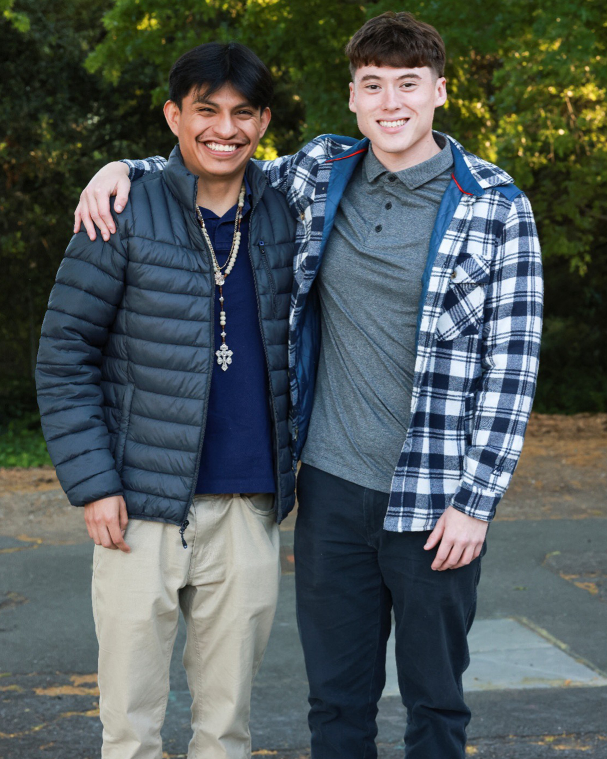 Two people posing together outdoors with trees in the background.